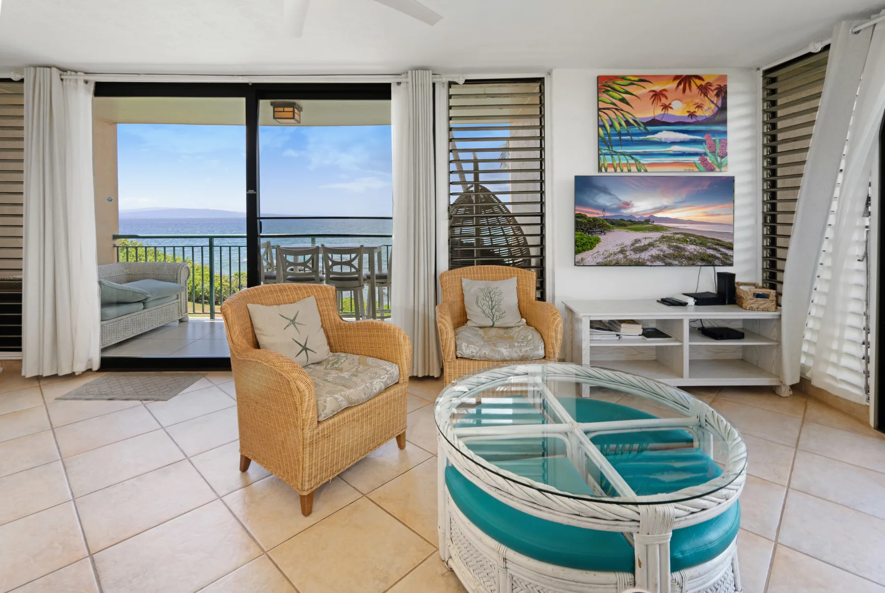 A bright living room with wicker seating, an oval glass coffee table, and ocean views.