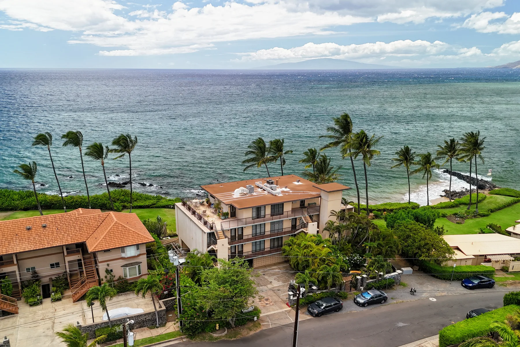 A coastal residential building overlooks the ocean, with palm trees along the shore.