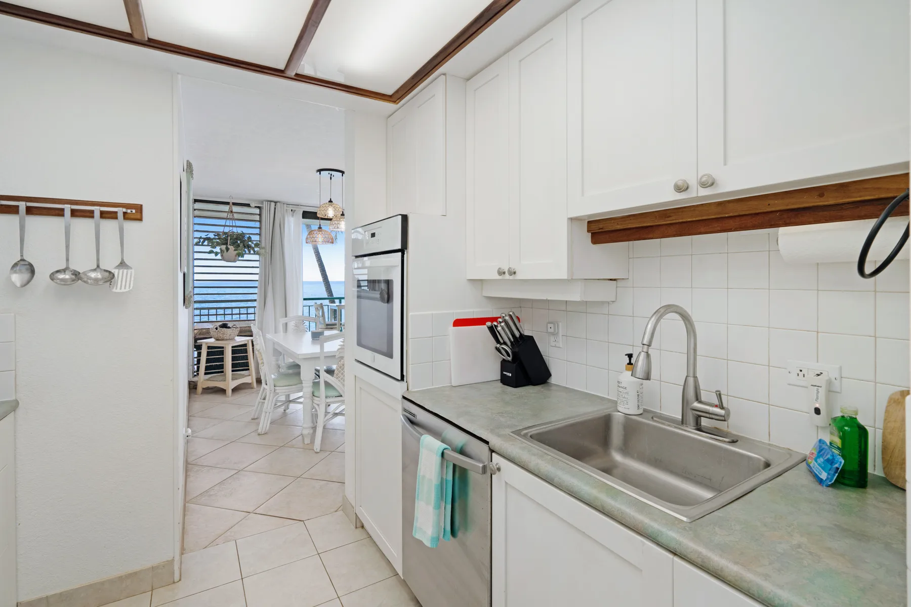 A bright kitchen with white cabinets, a sink, and a dining area visible beyond.