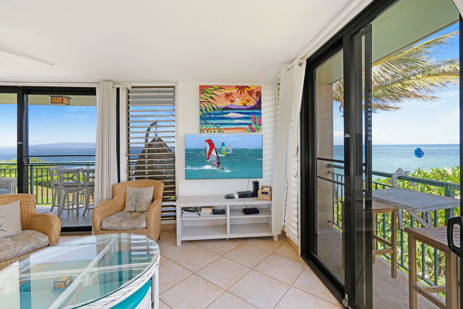 A bright living room opens onto a balcony, with ocean views through glass doors.