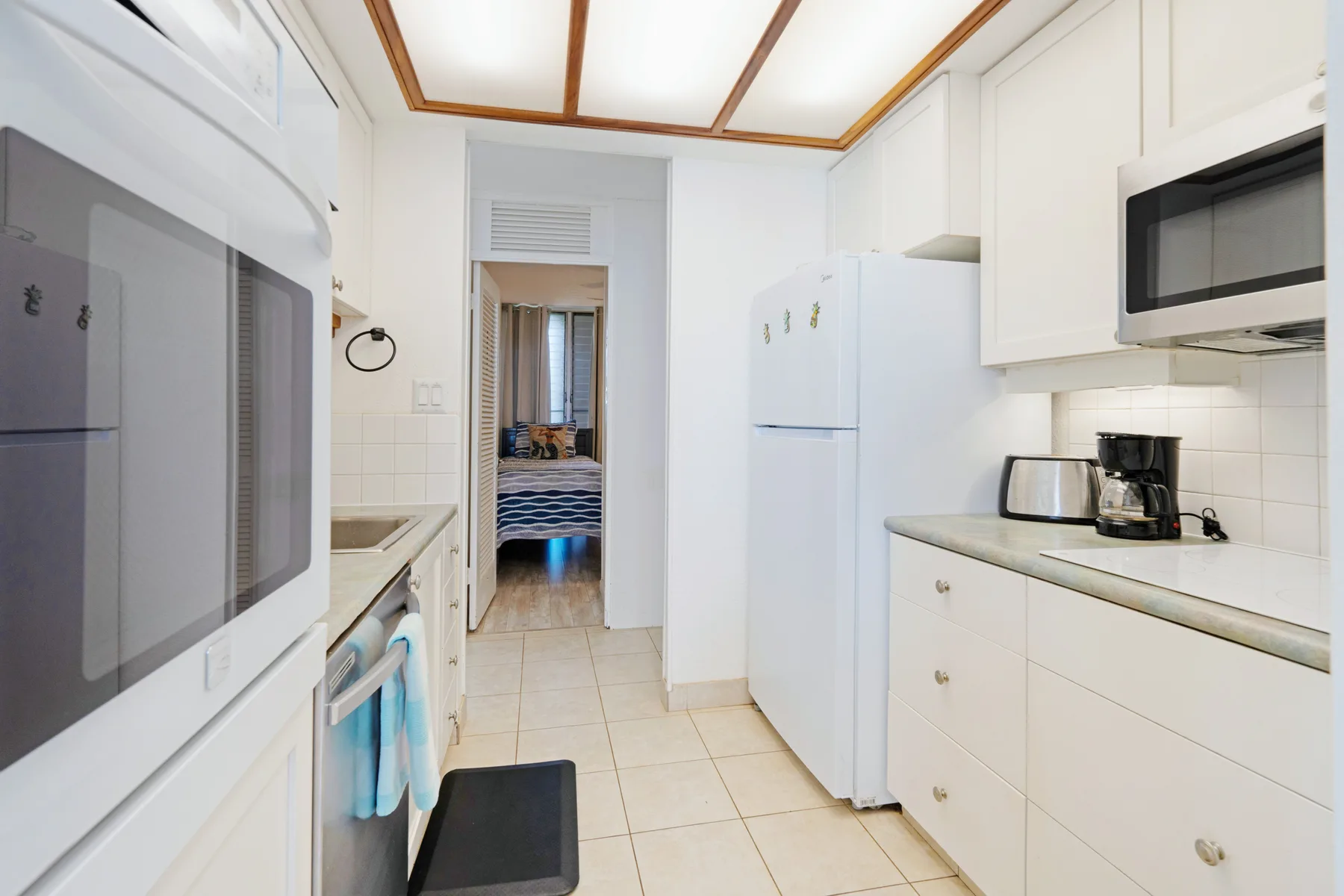 A bright white kitchen with tiled flooring, a refrigerator, and countertop appliances.