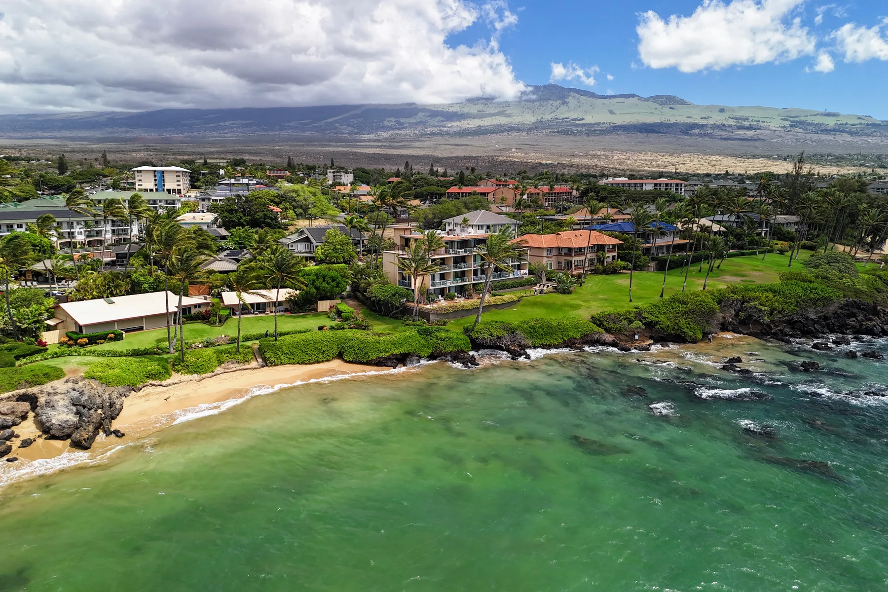 A coastal resort sits beside a sandy beach and green ocean water.
