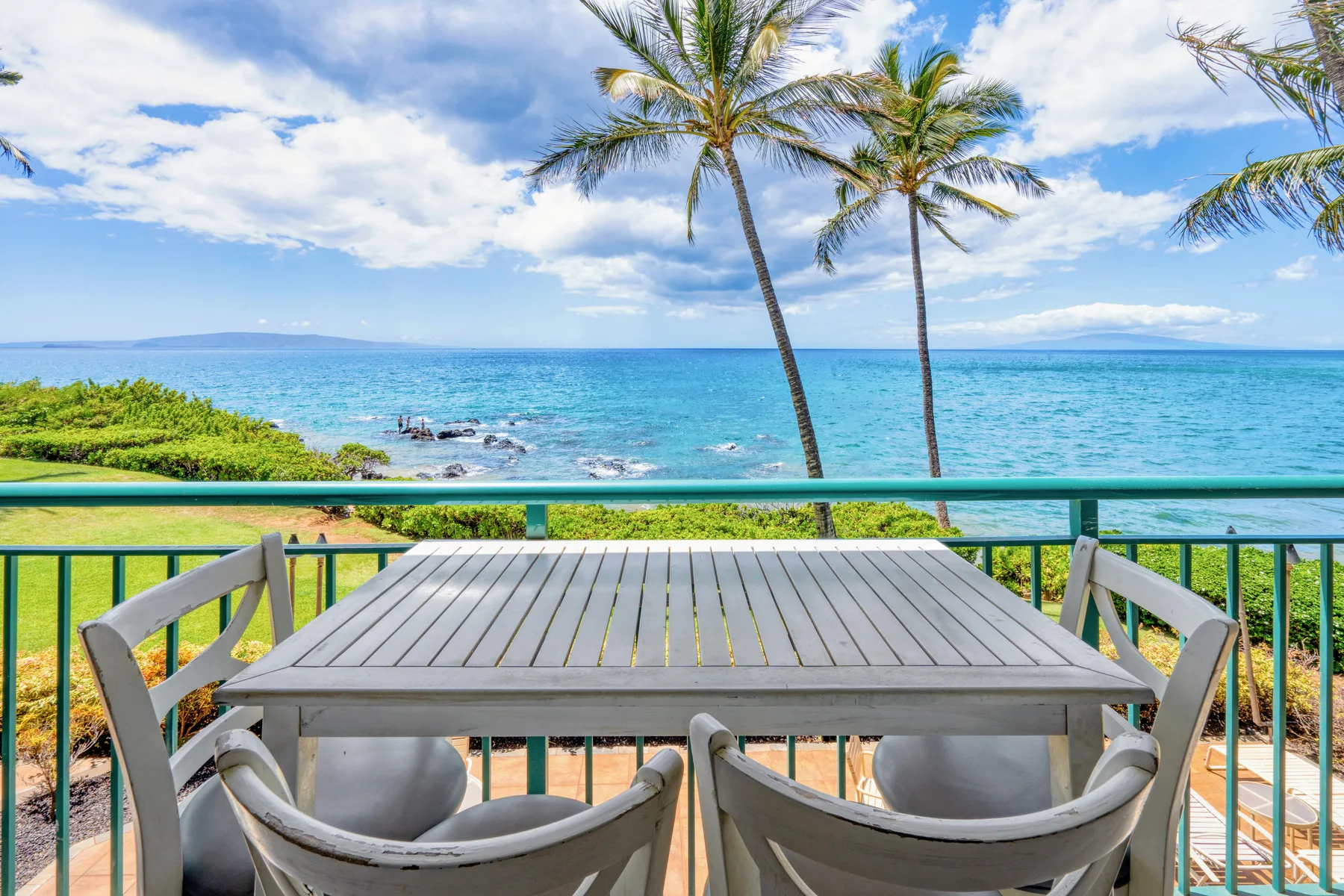 An outdoor dining area overlooks the ocean, with palm trees along the shore.