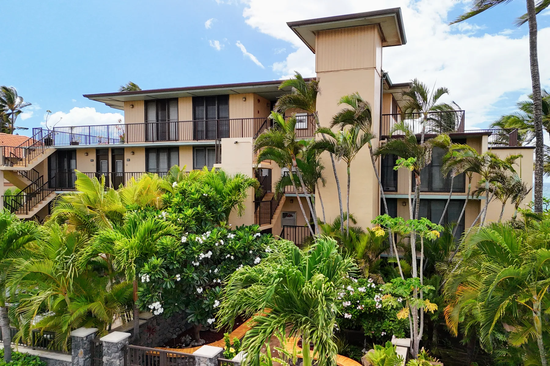 A multi-level building stands among palm trees and dense tropical landscaping.