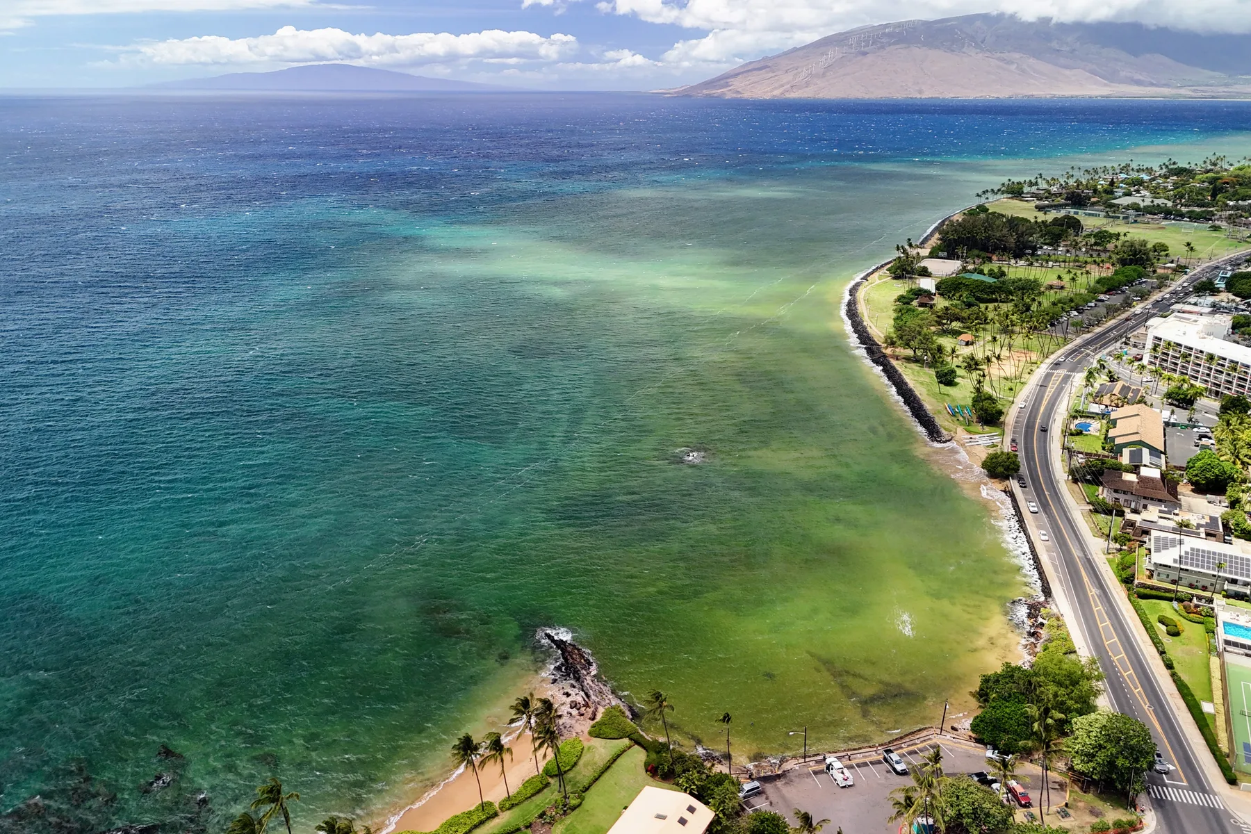 Aerial view of a curving coastline with turquoise water and a road along the shore.