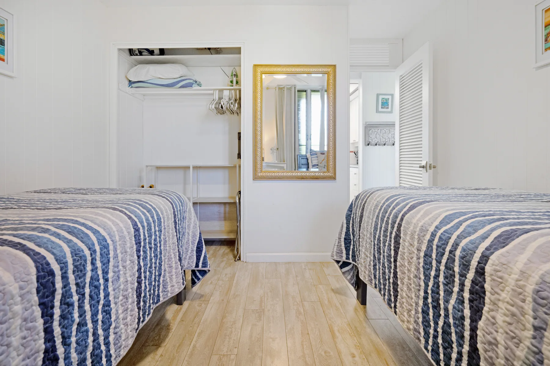 A bedroom with two beds, an open closet, and a mirror on the wall.