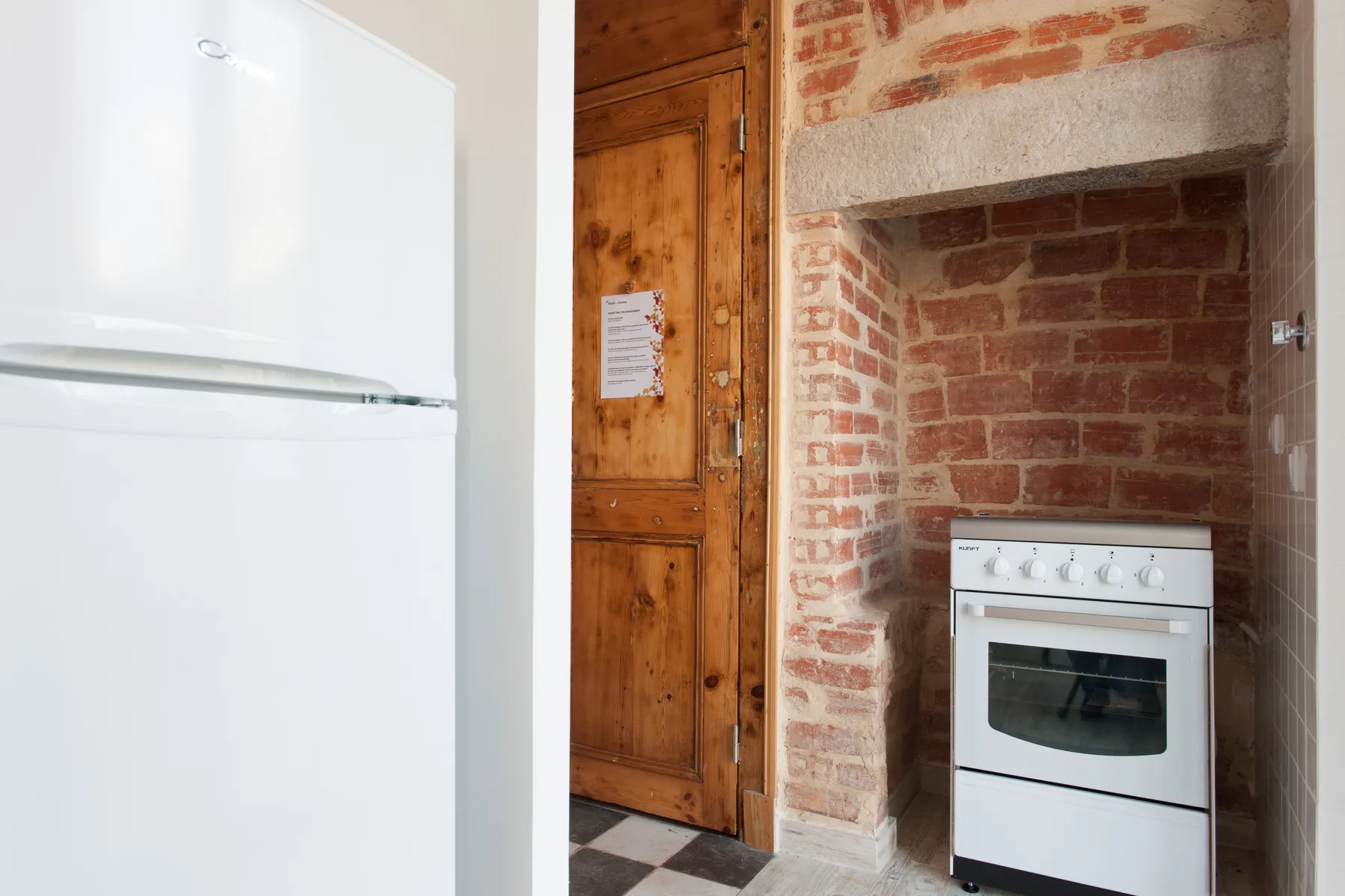 A kitchen with a refrigerator, oven, and exposed brick wall.