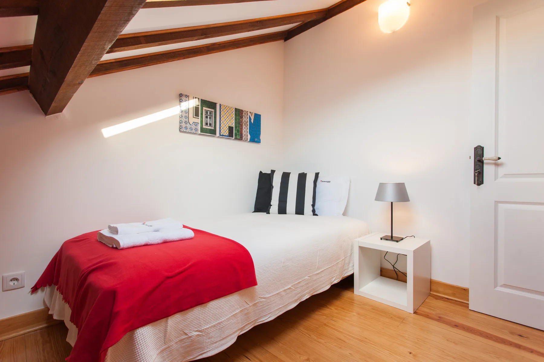 A bedroom with a bed dressed in white linens and a red cover.