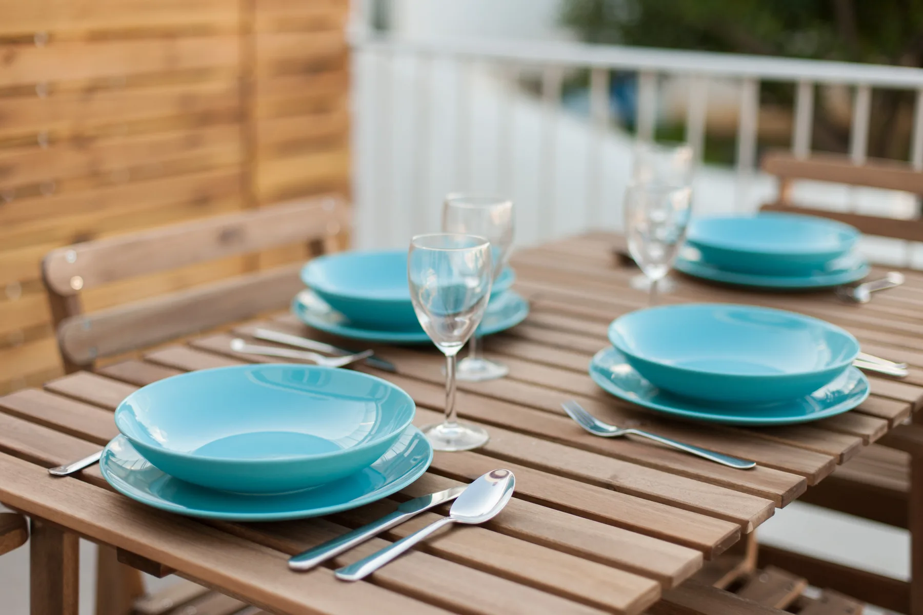 A dining table on a terrace is set with turquoise plates and glassware.