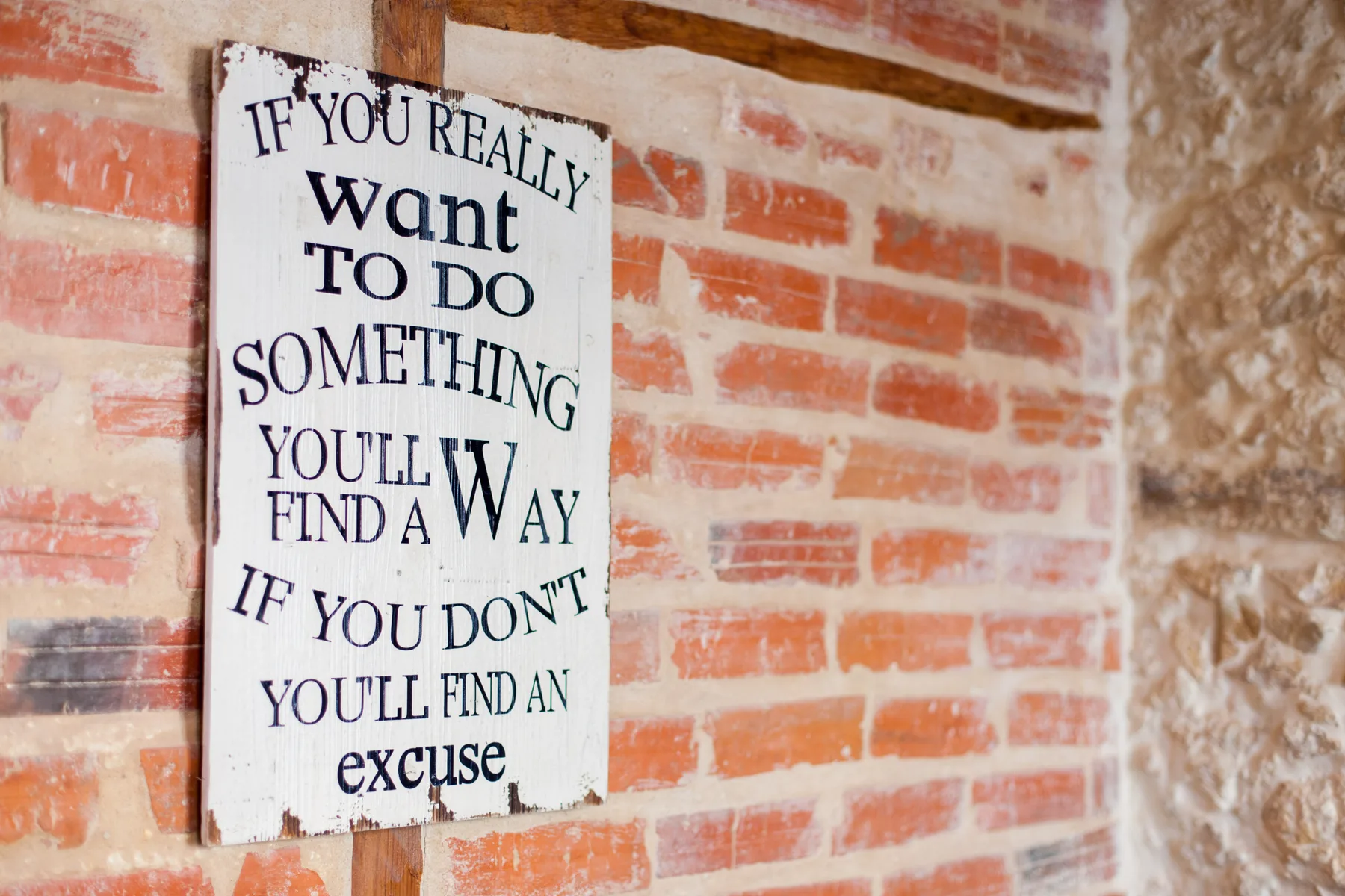 A motivational sign hangs on a brick wall.