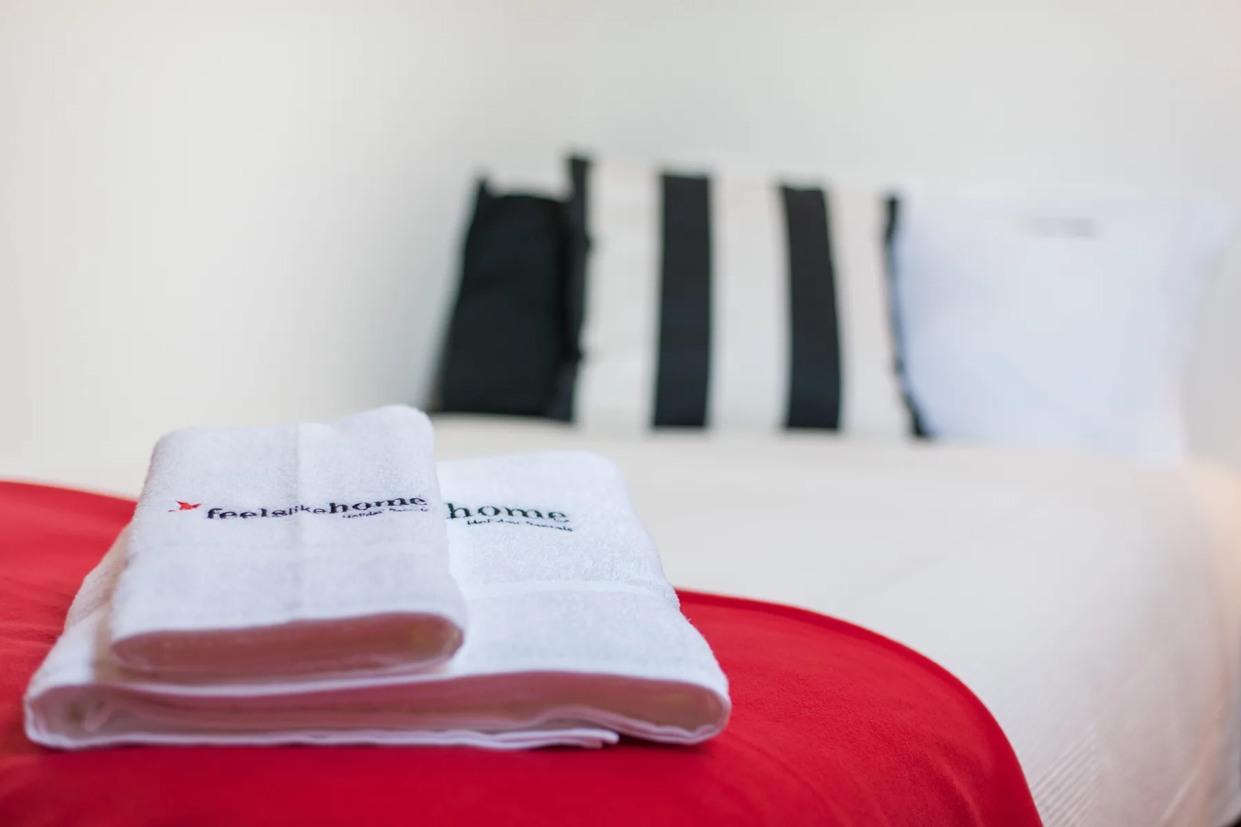 A bed with folded towels rests against black-and-white striped pillows.