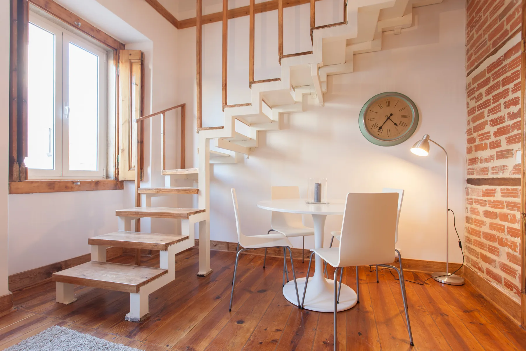 A dining area beneath a staircase, with a table and white seating.