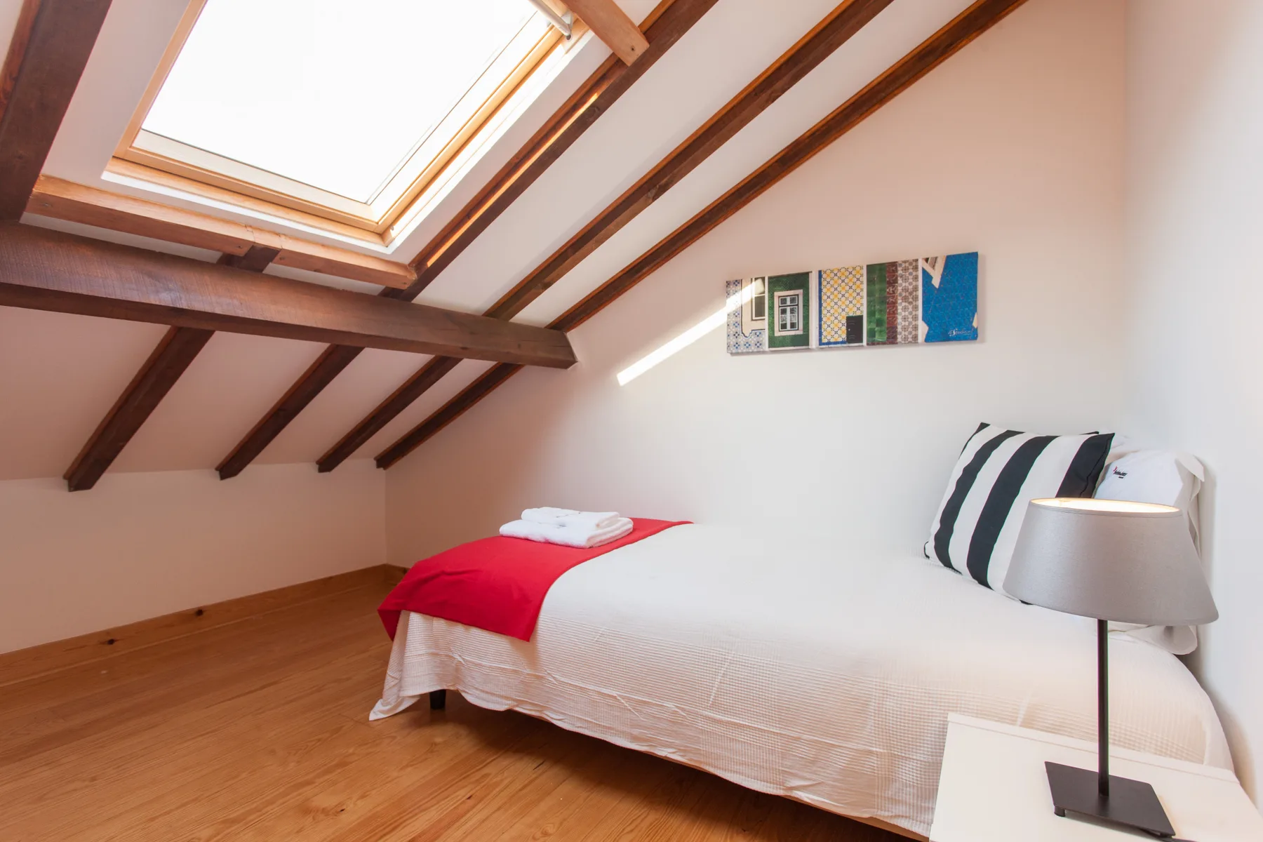 A bedroom with a bed beneath a sloped ceiling and skylight.