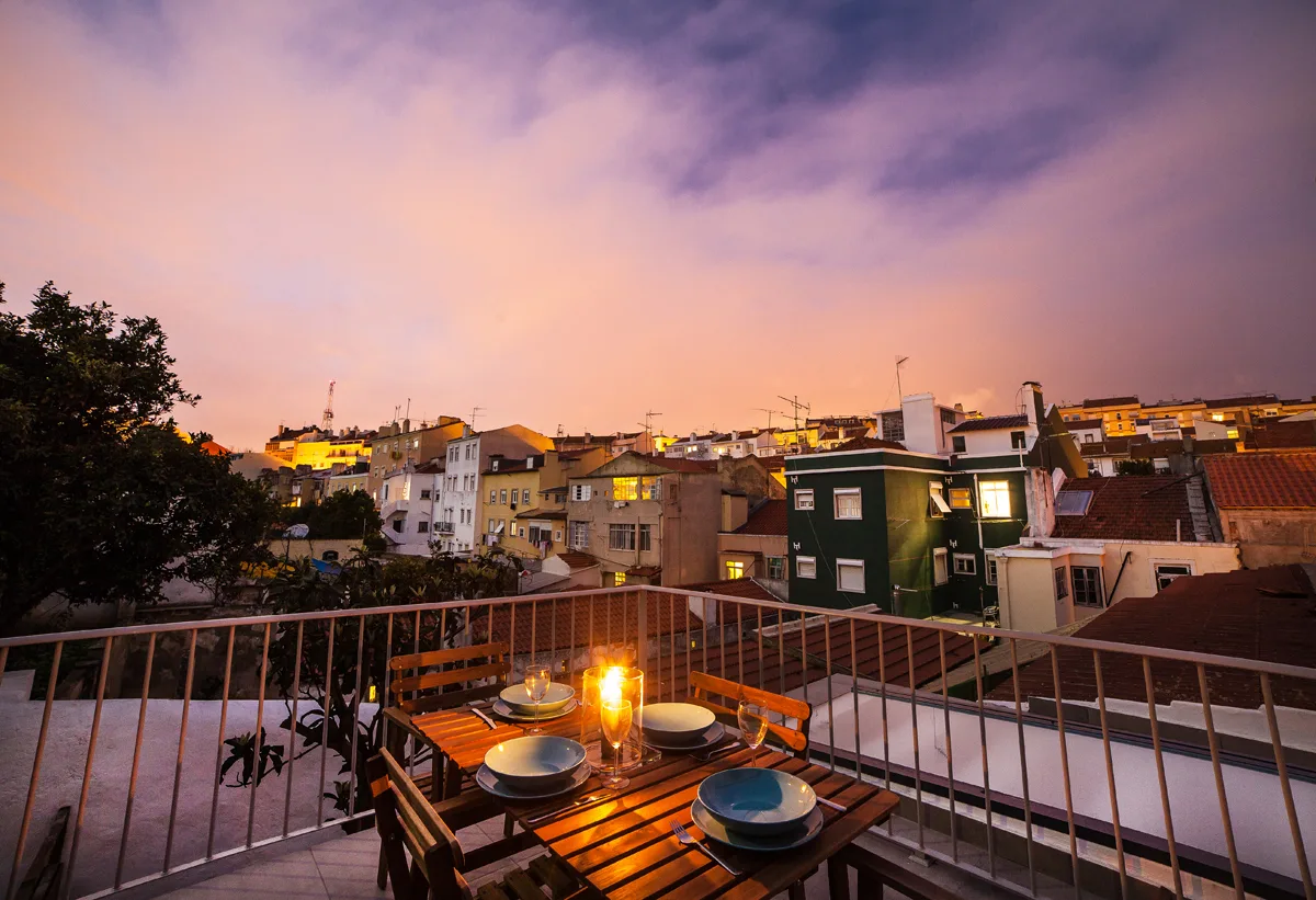 A rooftop terrace overlooks nearby buildings beneath a colorful sunset sky.