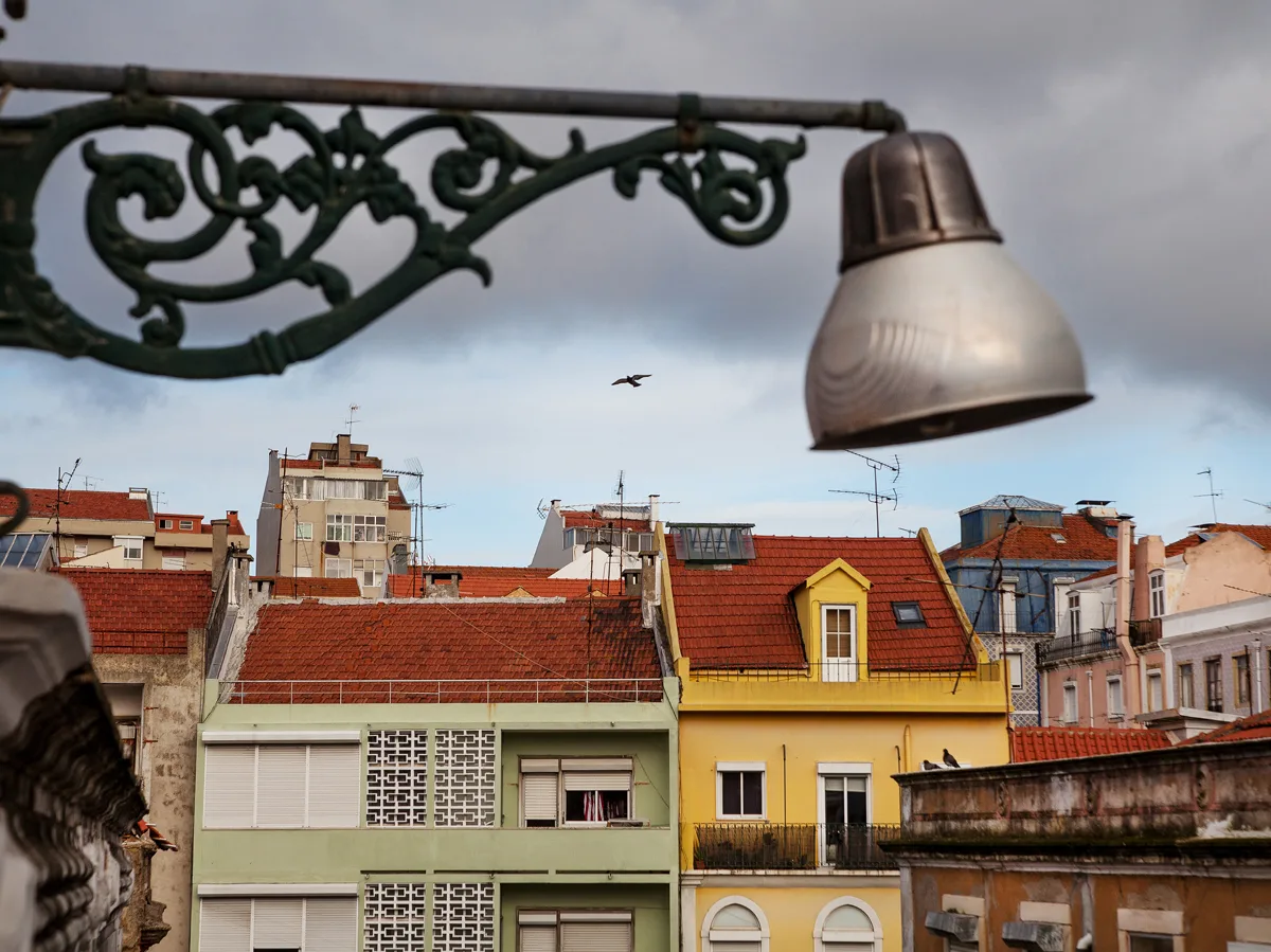 A row of colorful urban buildings with red-tiled roofs is seen beneath a cloudy sky.