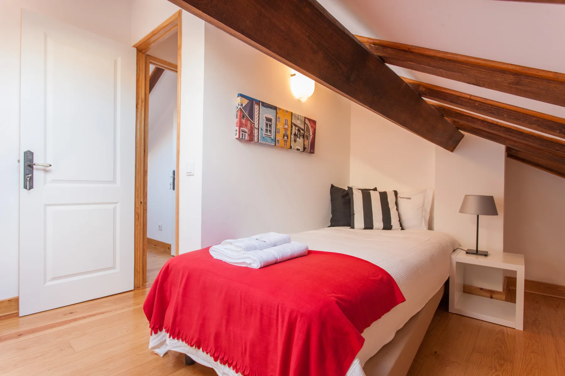 A bedroom with a bed dressed in white and a red blanket.