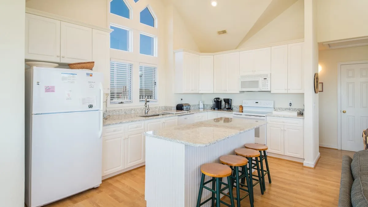 A bright kitchen with white cabinetry, a central island, and bar seating.
