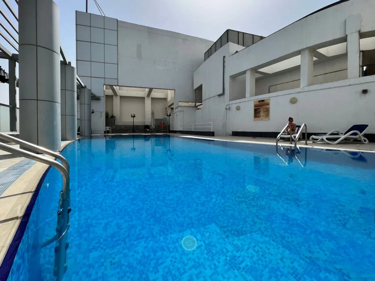 An outdoor swimming pool beside a modern white building, with lounge chairs along the edge.