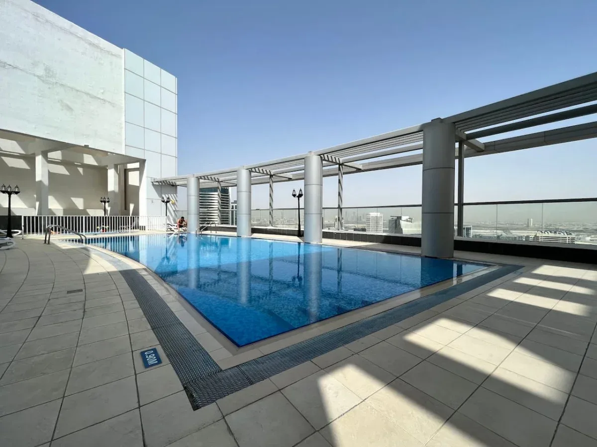 A rooftop swimming pool sits beside a paved terrace beneath a clear sky.