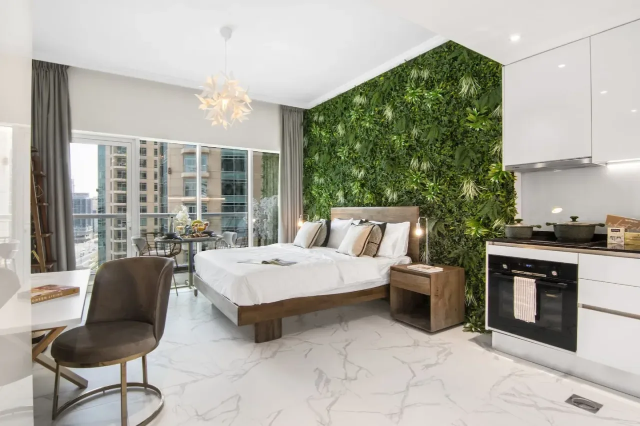 Bedroom with a bed beside a green plant-covered wall and a compact kitchen.