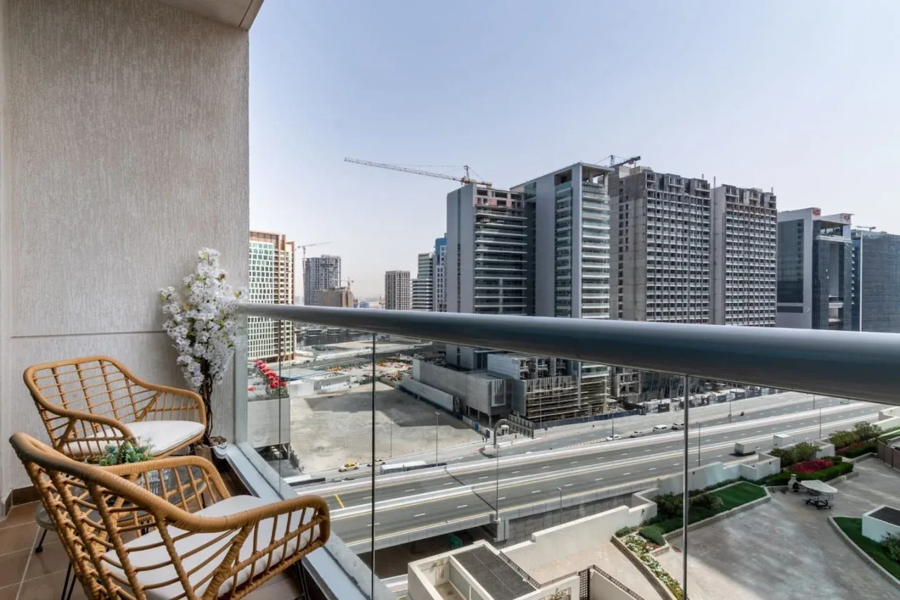 A balcony with wicker seating overlooks a city street and nearby buildings.