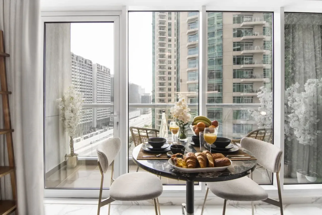 A dining area with a table set with dishes and pastries beside large windows.