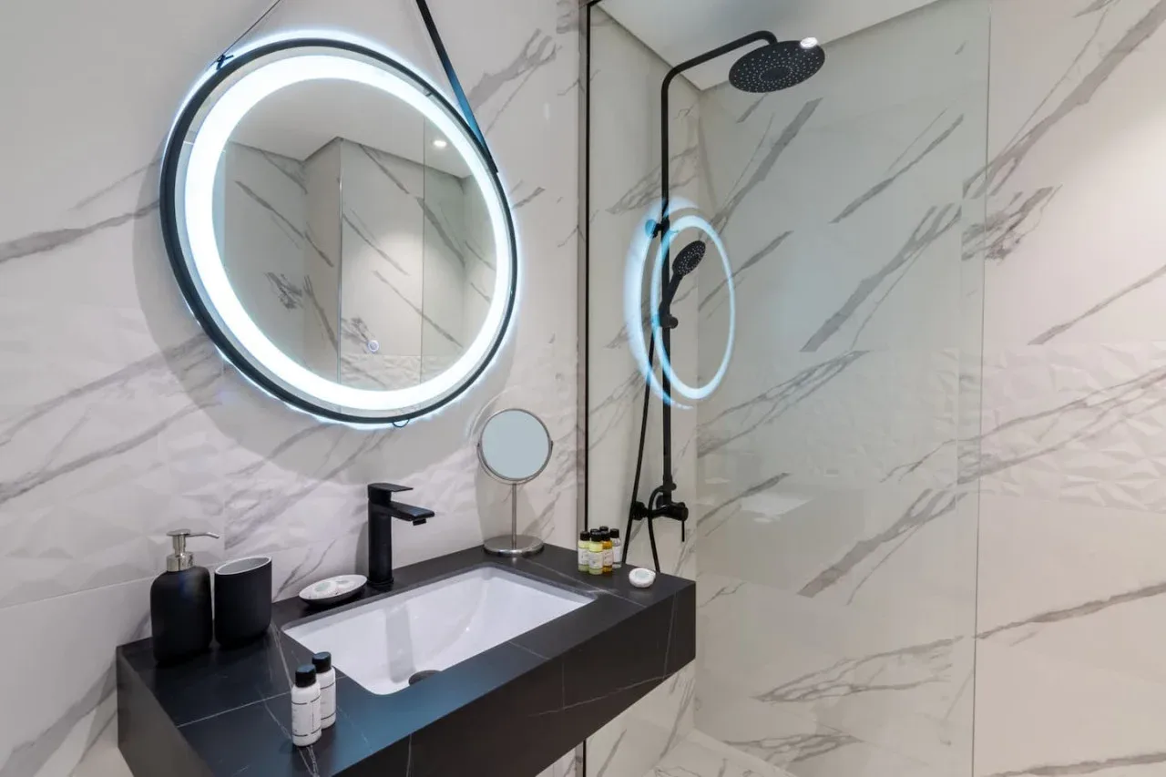A modern bathroom with a wall-mounted sink, illuminated mirror, and shower.