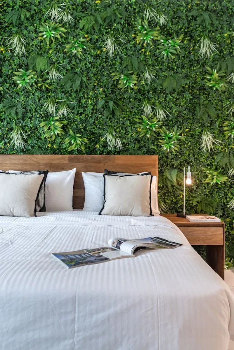 A bedroom with white bedding and a leafy green wall behind the bed.