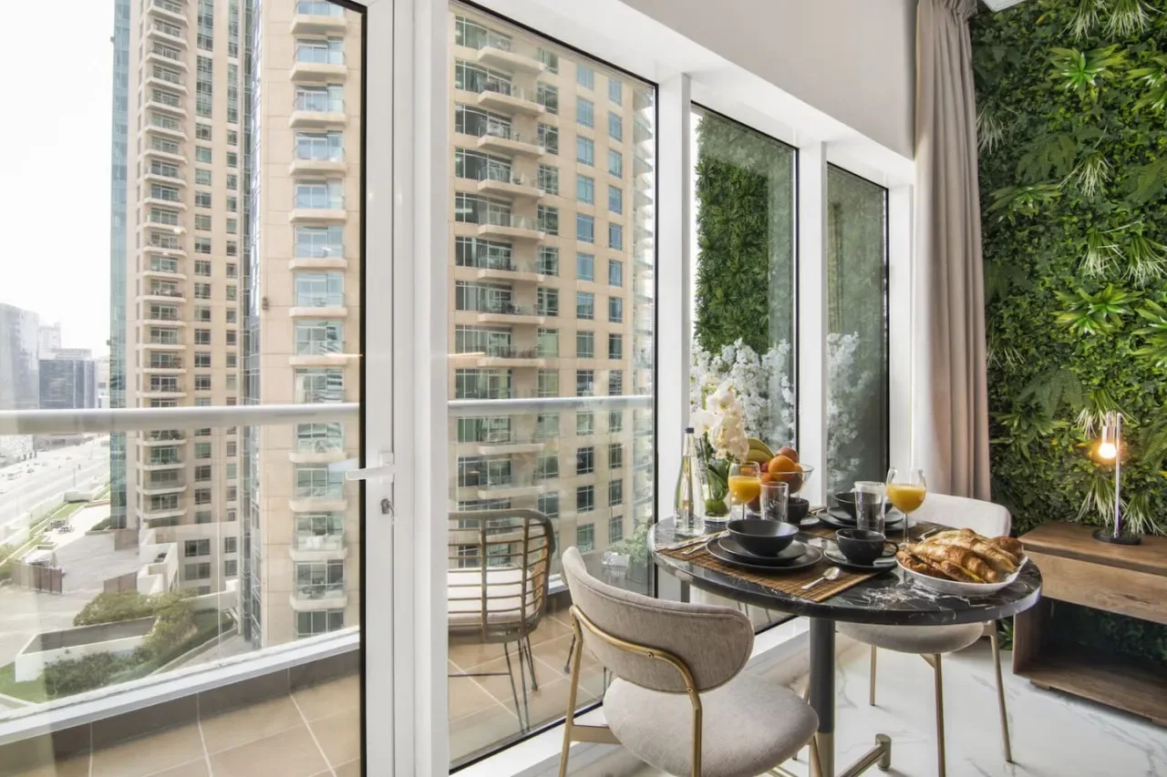 A dining area with a set table beside large windows overlooking nearby buildings.