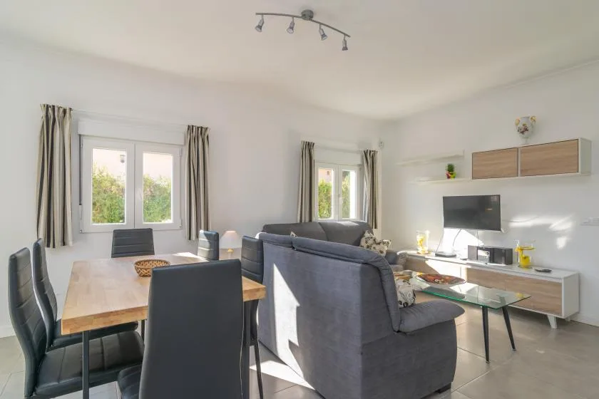 A bright living and dining room with a gray seating area and wooden dining table.