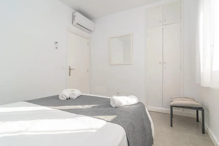 A bright bedroom with white bedding, a gray bedspread, and a window.