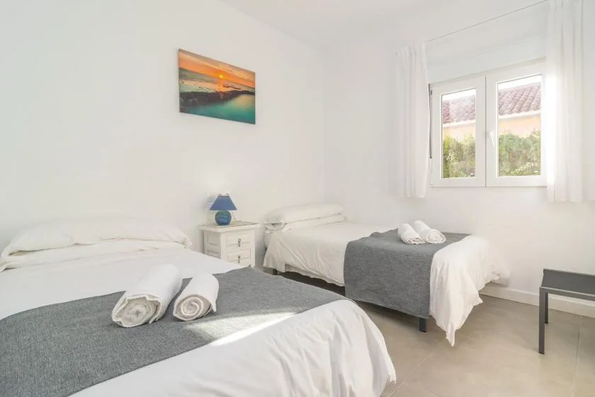 A bright bedroom with two beds, a bedside table, and a window.