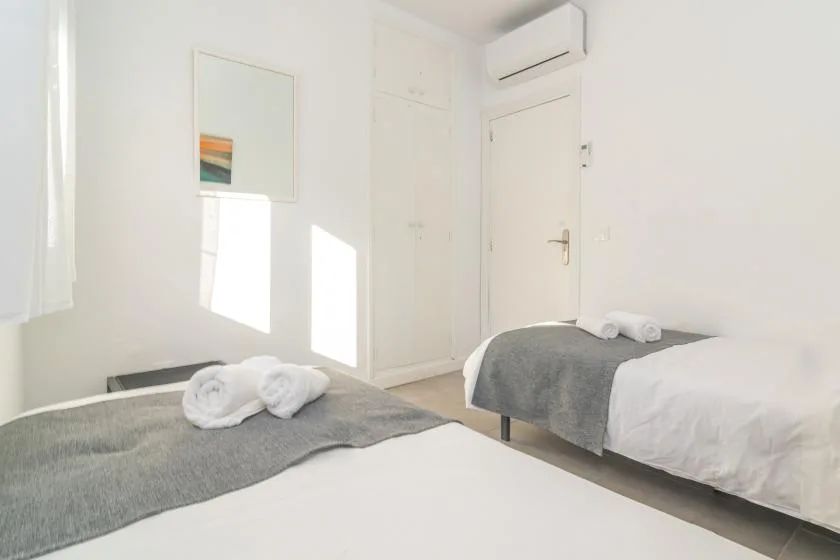 A bright bedroom with two beds covered in white and gray bedding.
