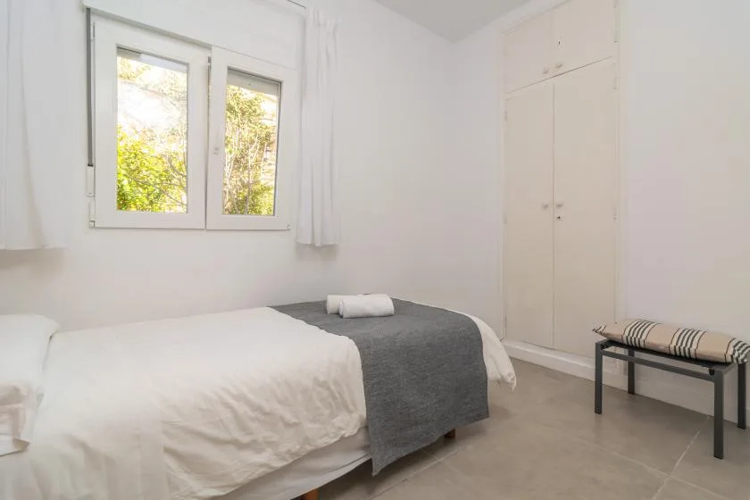 A bright bedroom with a bed beneath a window and a built-in wardrobe.