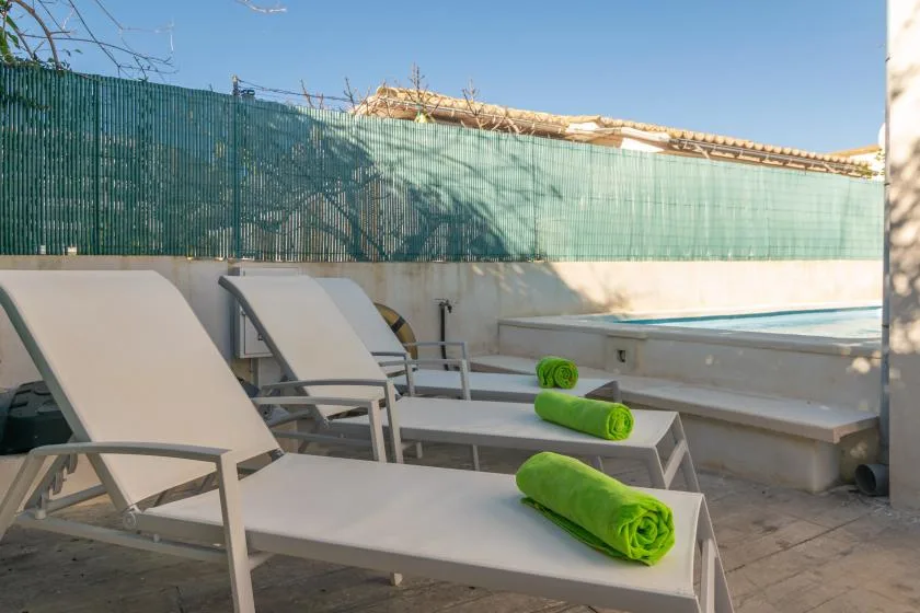 A sunlit outdoor poolside seating area with lounge chairs and green towels.