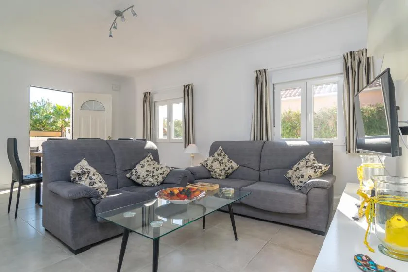 A bright living room with an L-shaped seating area and glass coffee table.