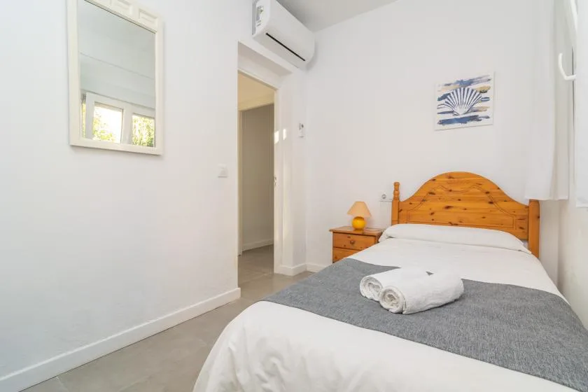A bright bedroom with a bed, folded towels, and a bedside lamp.