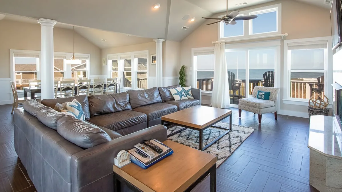 A bright living room with a large seating area beside expansive windows.