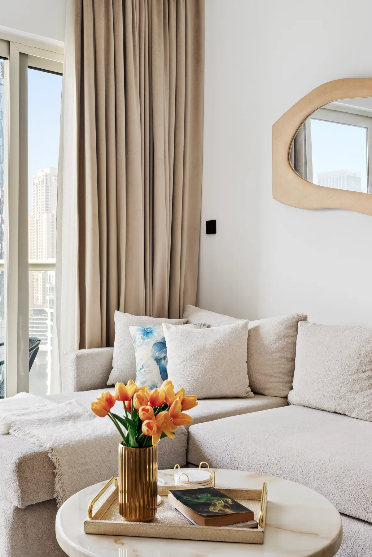 Una sala luminosa con un sofá seccional beige y un jarrón de flores naranjas.