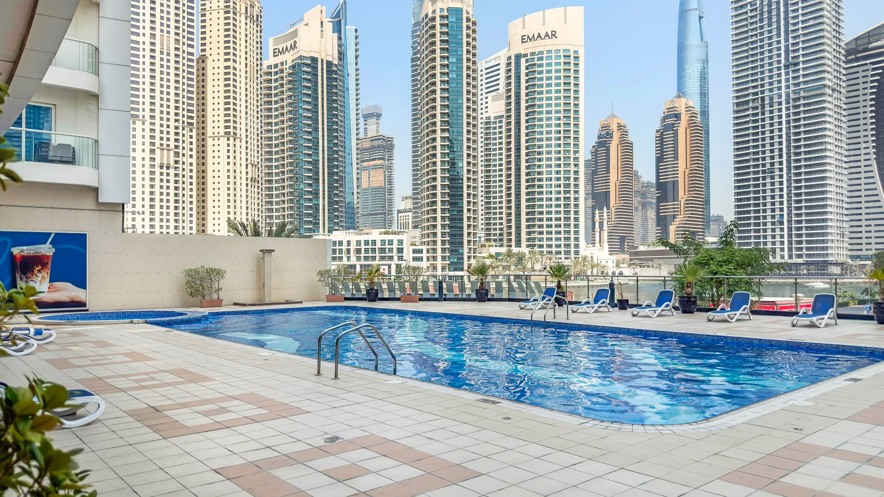 Una piscina al aire libre y una terraza embaldosada se encuentran frente al horizonte urbano.