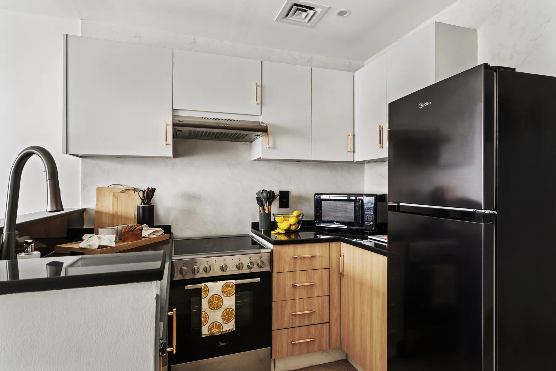 Una cocina compacta con gabinetes blancos, una estufa y un refrigerador grande.