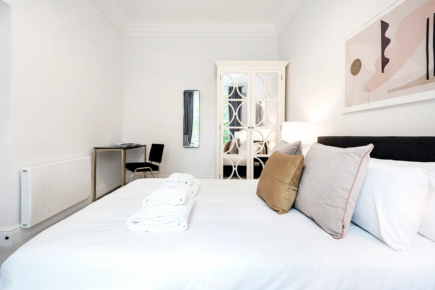 Un dormitorio luminoso con una cama bien hecha y un armario con espejo.