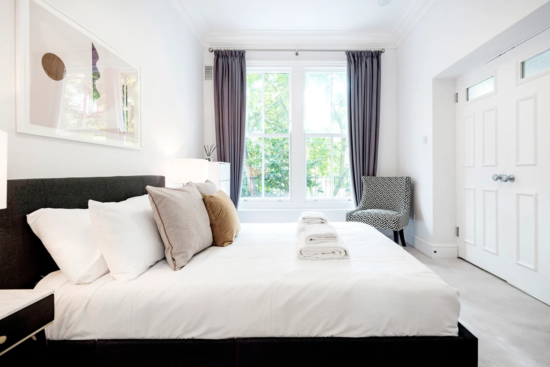 Un dormitorio luminoso con una cama tendida y ventanas altas.