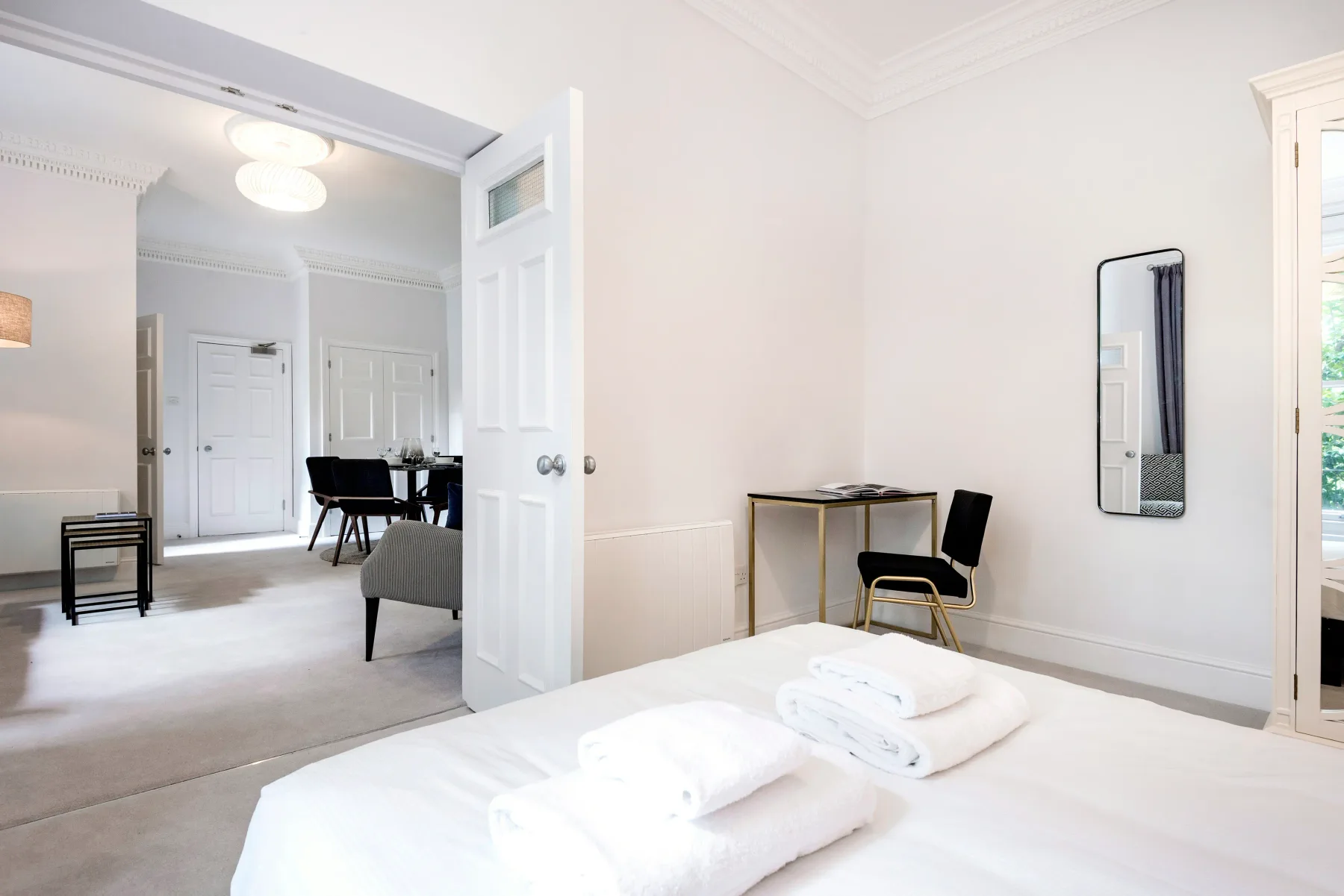 Un dormitorio luminoso con toallas dobladas sobre la cama y un pequeño escritorio junto a la pared.