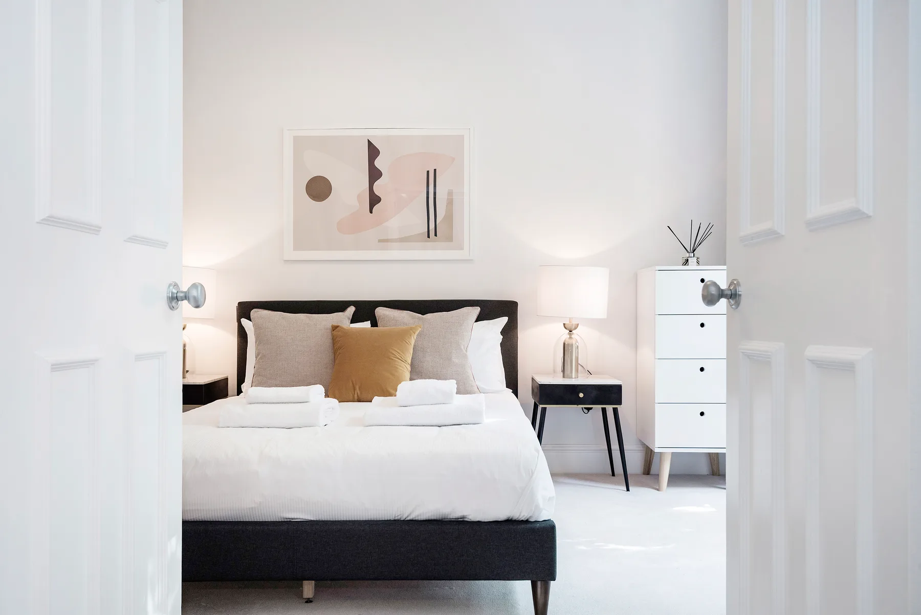 A bright bedroom with a neatly made bed and framed artwork above it.