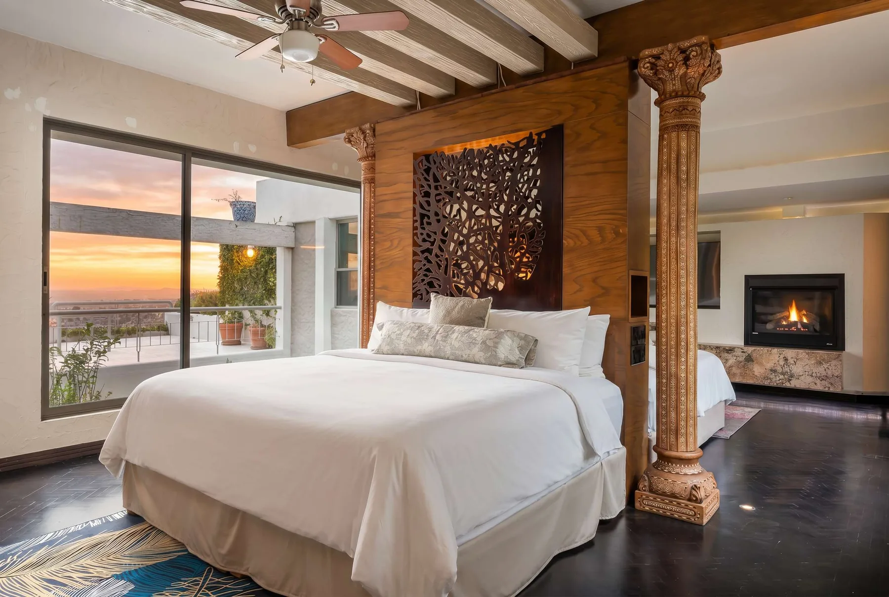 A bedroom with a neatly made bed, carved wood accents, and a fireplace.
