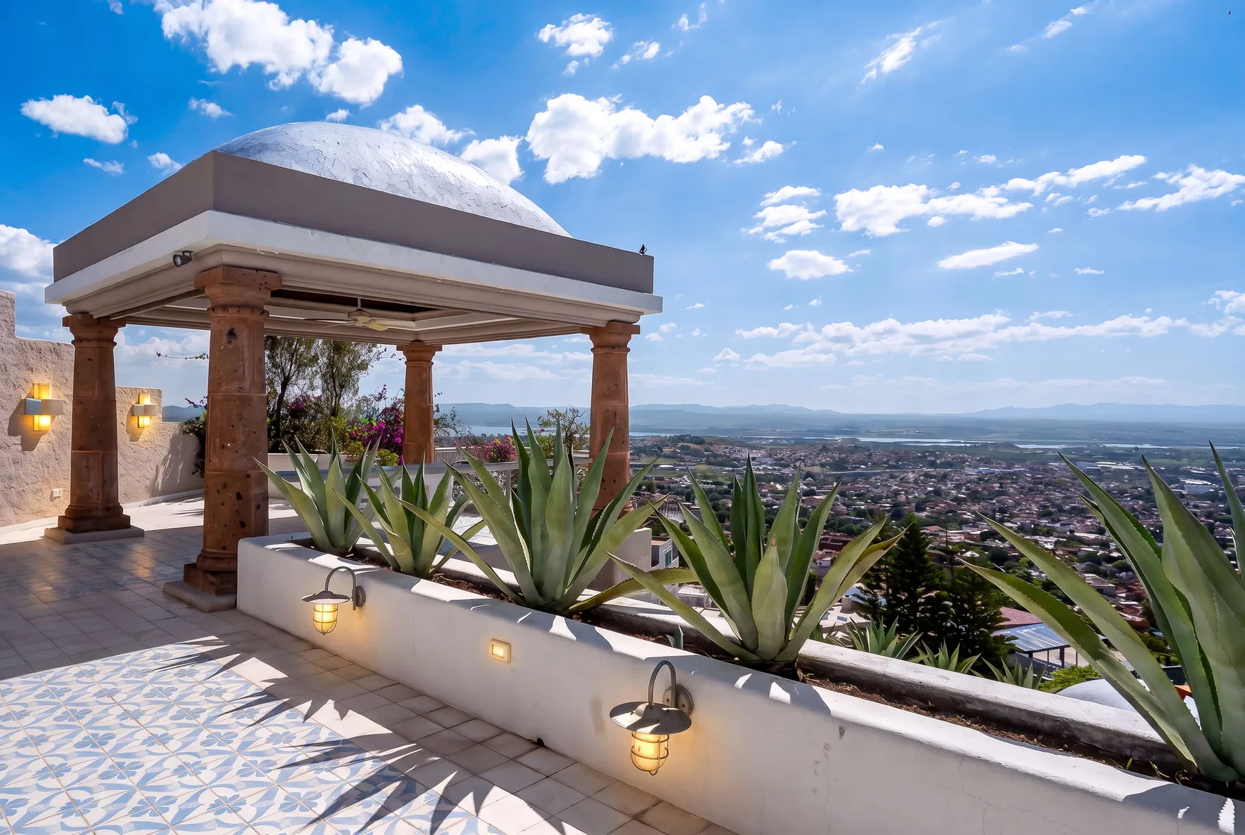 Una terraza en la azotea con una pérgola sombreada domina una ciudad y colinas lejanas.