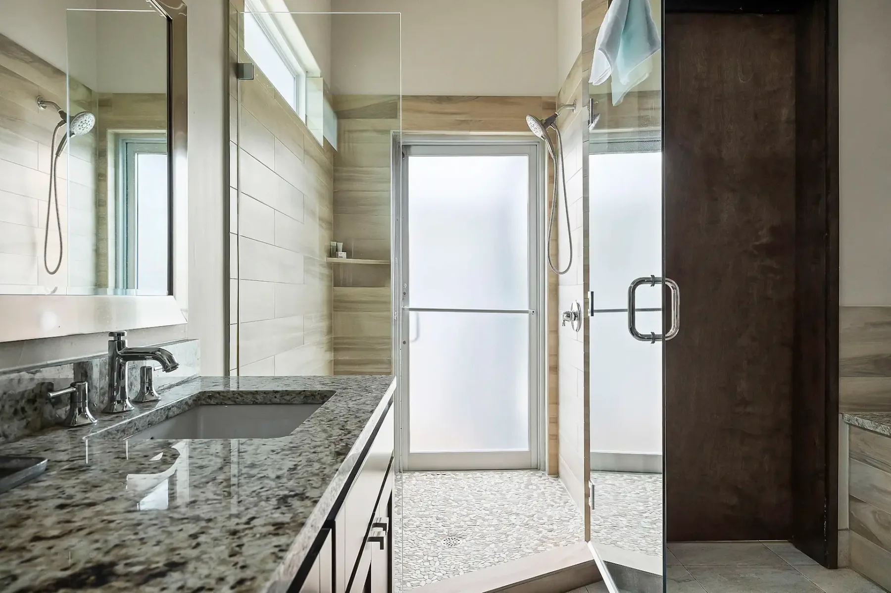 Un baño luminoso con una larga encimera de piedra, un lavabo visible y una ducha de vidrio.