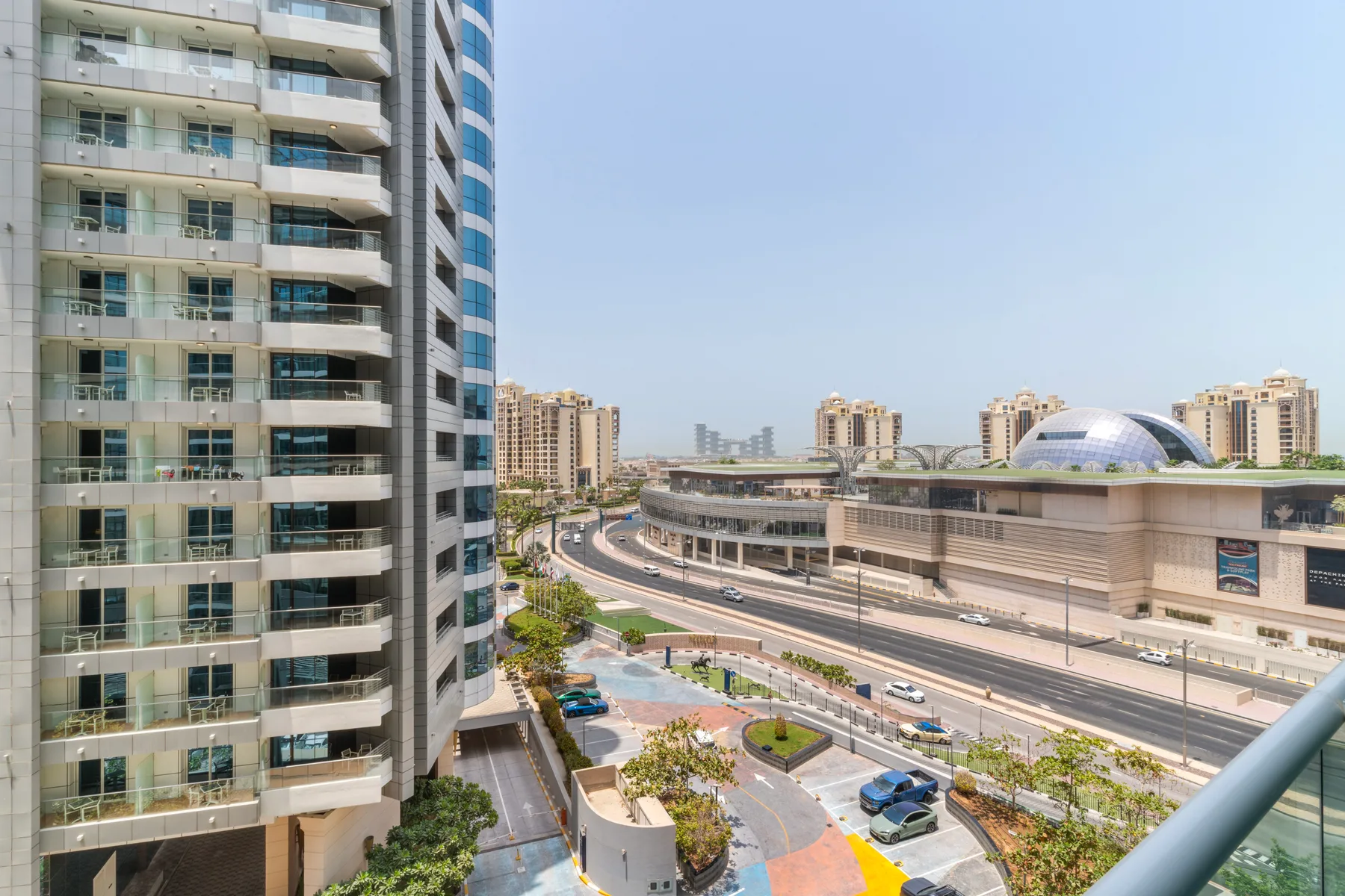Un paisaje urbano con una carretera curva, una plaza ajardinada y edificios modernos.