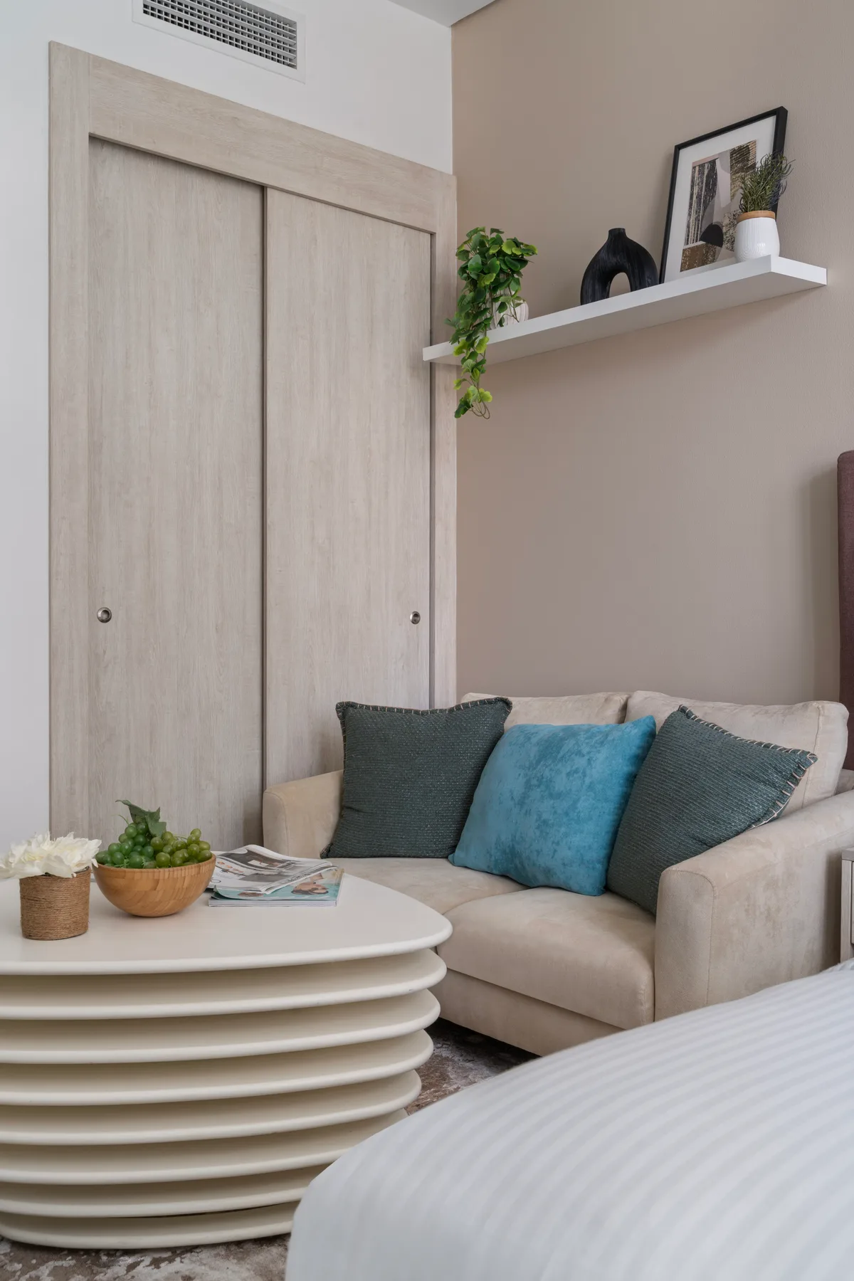 Un rincón de estar en un dormitorio con sofá, mesa de centro y estante de pared.